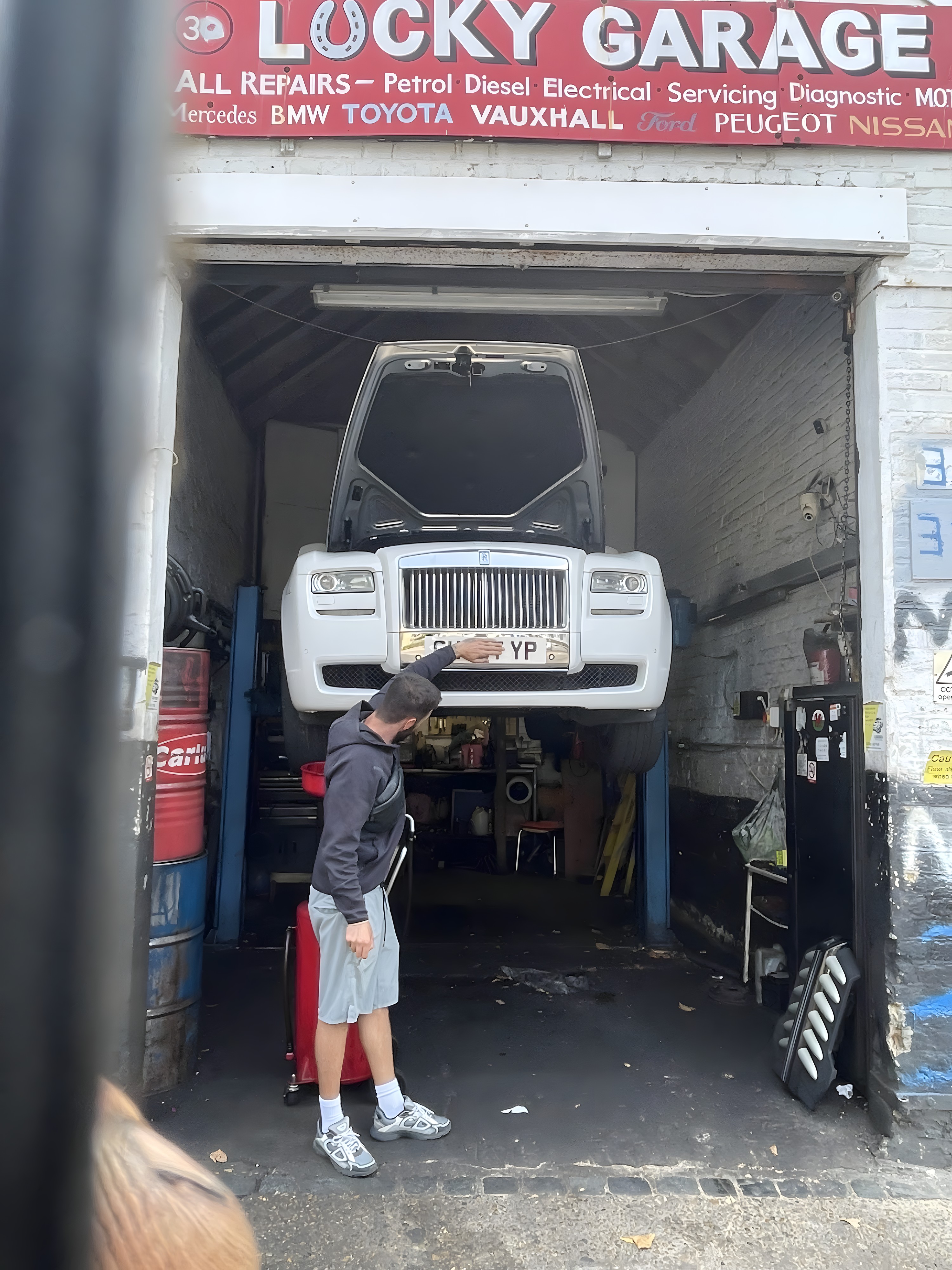 A white Rolls-Royce raised on the ramp inside Lucky Garage on Morris Road, under the workshop sign